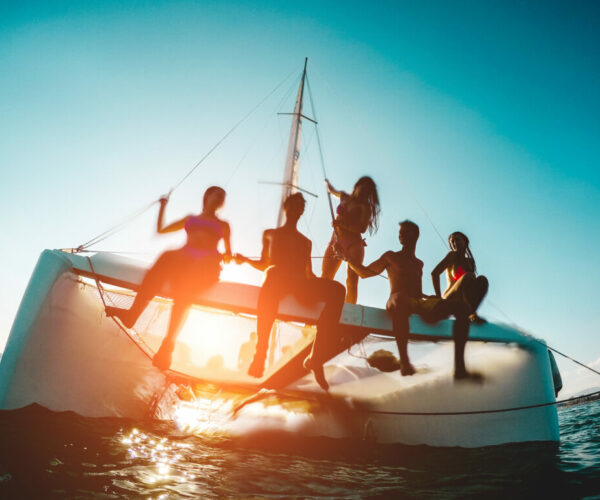Silhouette of young friends chilling in private catamaran boat -